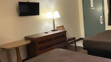 A hotel room with a bed, a desk with a lamp, a television, and a door with a "No Smoking" sign.