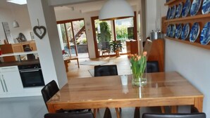 A modern dining area with a wooden table and black chairs, a vase with flowers, and a view of the outdoor patio. - Large vacation apartment in the beautiful Ruwer valley (Kasel)