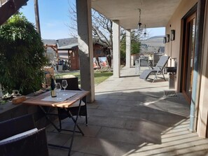 A covered patio with a table set for two, a chair, and a bottle of wine.