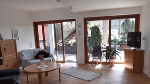 A spacious living room with a sofa, a coffee table, and a TV stand. There are large sliding glass doors leading to an outdoor area with a staircase. - Large vacation apartment in the beautiful Ruwer valley (Kasel)