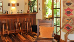 A bar area with wooden stools, a bar counter, and a ceiling fan. - HUGE! Belize Vacation Lodge, 1 to 6 Private Cottages Plus Fully Equipped Kitchen (Punta Gorda)