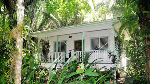 Um edifício branco com varanda rodeado por vegetação exuberante.
