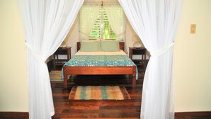 A bedroom with a wooden bed, white curtains, and a green patterned bedspread. - HUGE! Belize Vacation Lodge, 1 to 6 Private Cottages Plus Fully Equipped Kitchen (Punta Gorda)