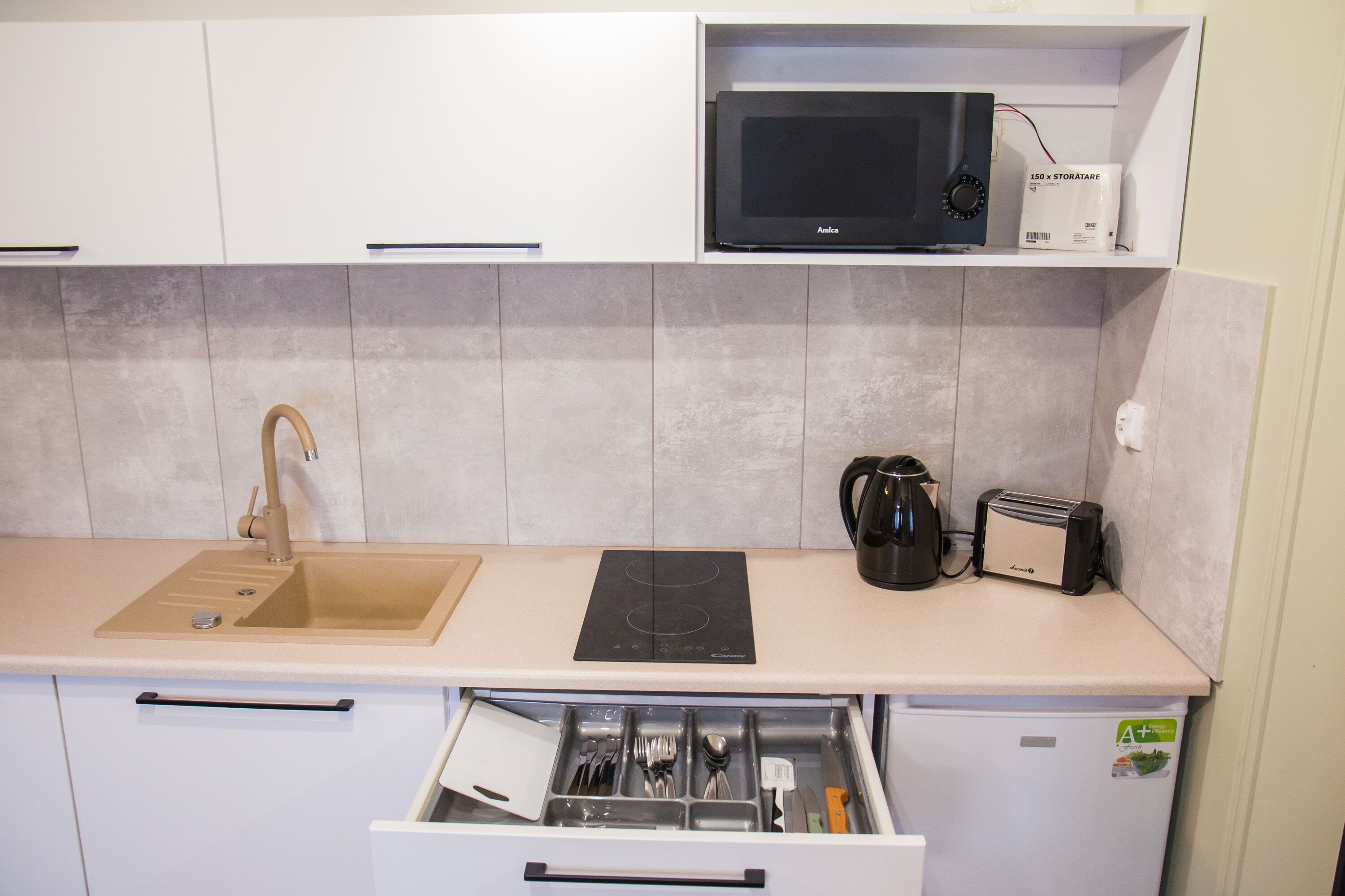 A compact kitchen with a sink, microwave, toaster, and a drawer with utensils.