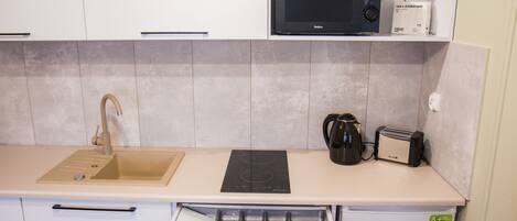 A compact kitchen with a sink, microwave, toaster, and a drawer with utensils.
