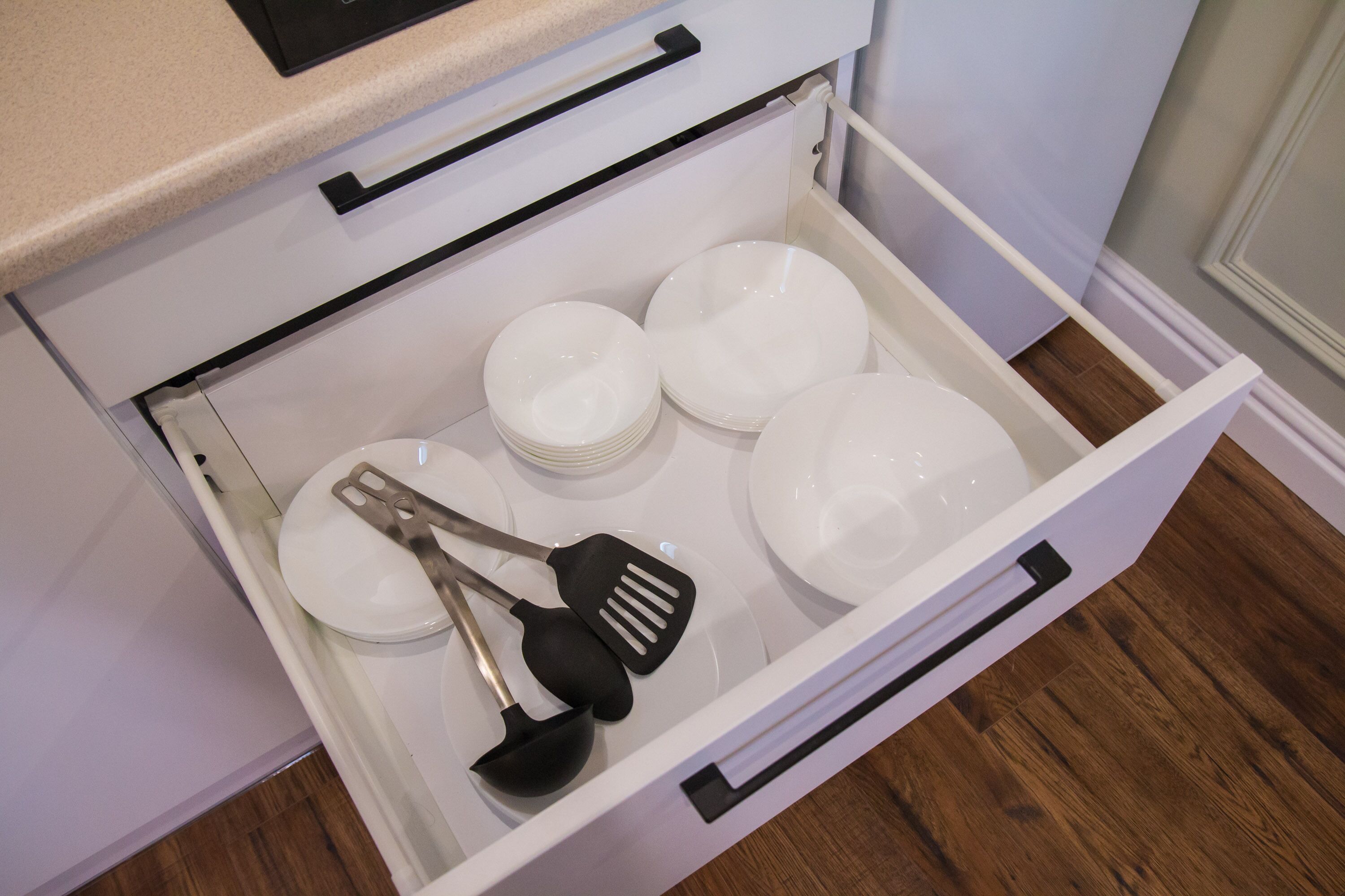 A kitchen drawer containing white plates, bowls, and kitchen utensils.
