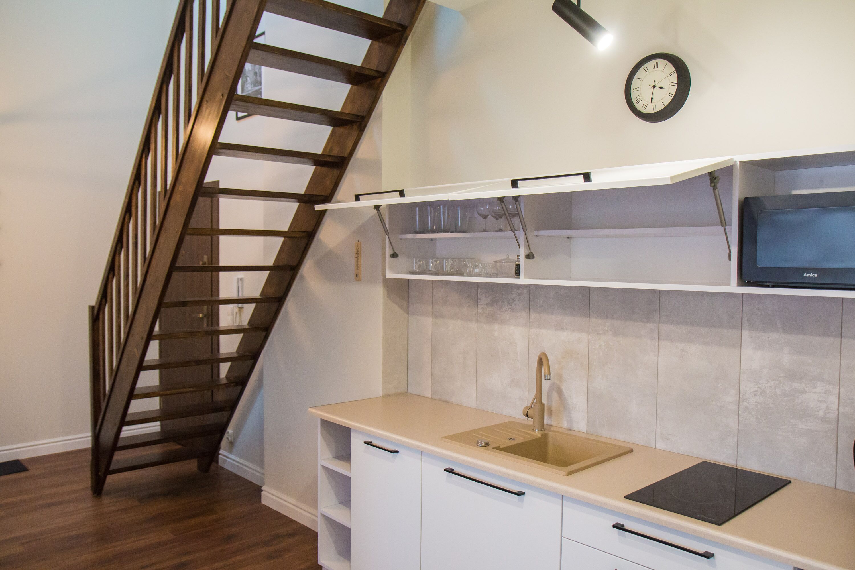 Cocina con escalera de madera, pileta, alacenas y microondas.