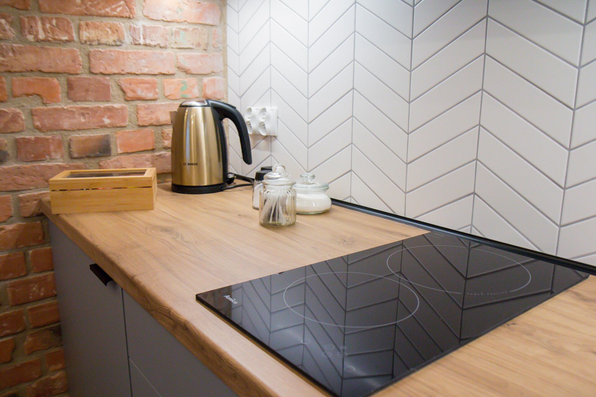A kitchen with a brick wall, a Bosch kettle, a glass jar, and a black induction cooktop.