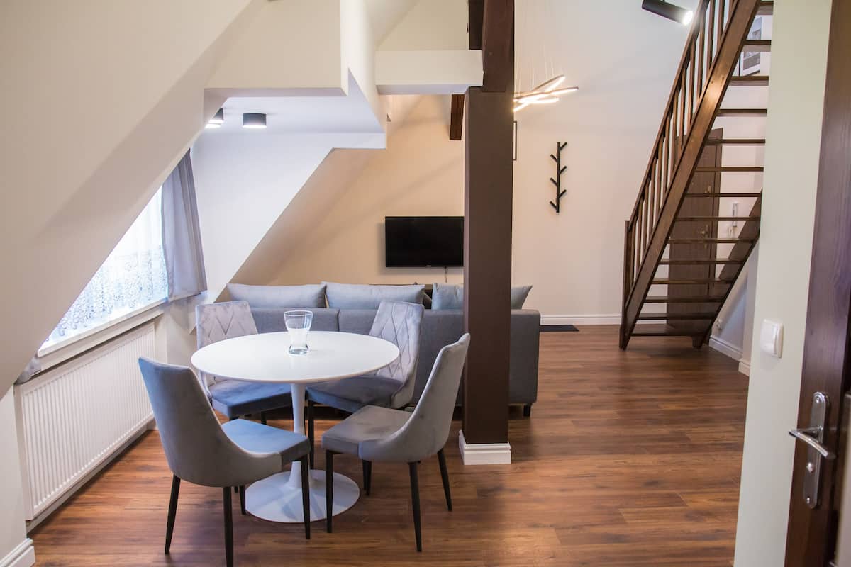 A modern loft-style room with a dining area, a gray sofa, and a staircase.