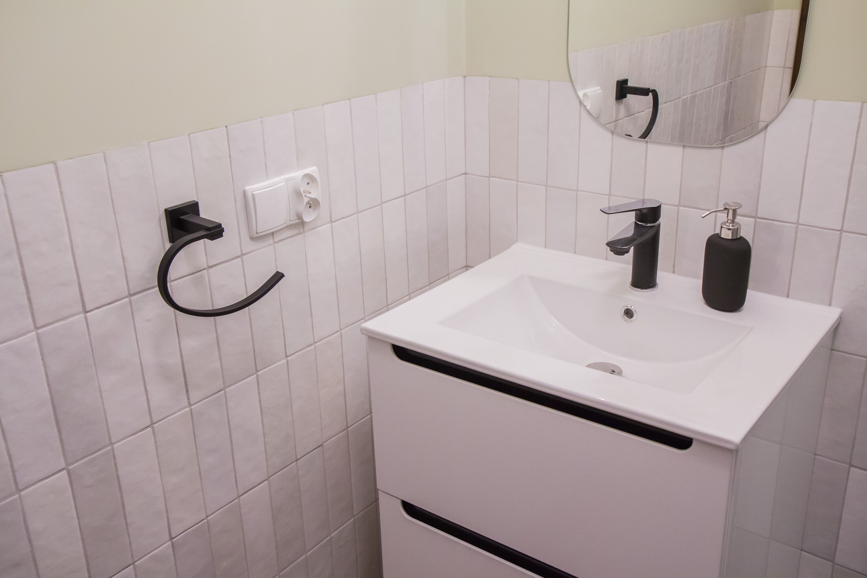 Un baño con un lavamanos blanco, un grifo negro y un espejo encima.