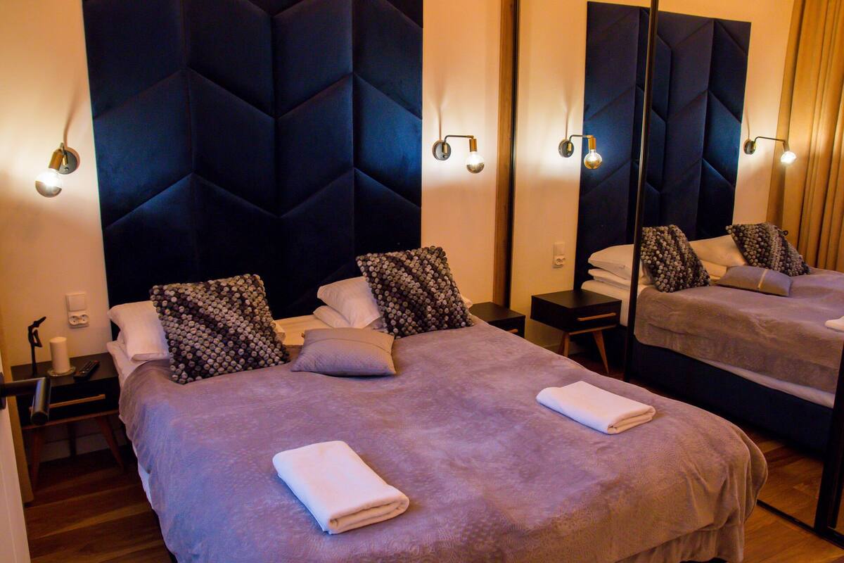 A hotel room with two beds, each with a headboard, bedside tables, and a mirror.