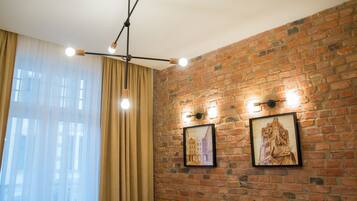 A room with a brick wall, two framed pictures, a hanging light fixture, and a window with curtains.