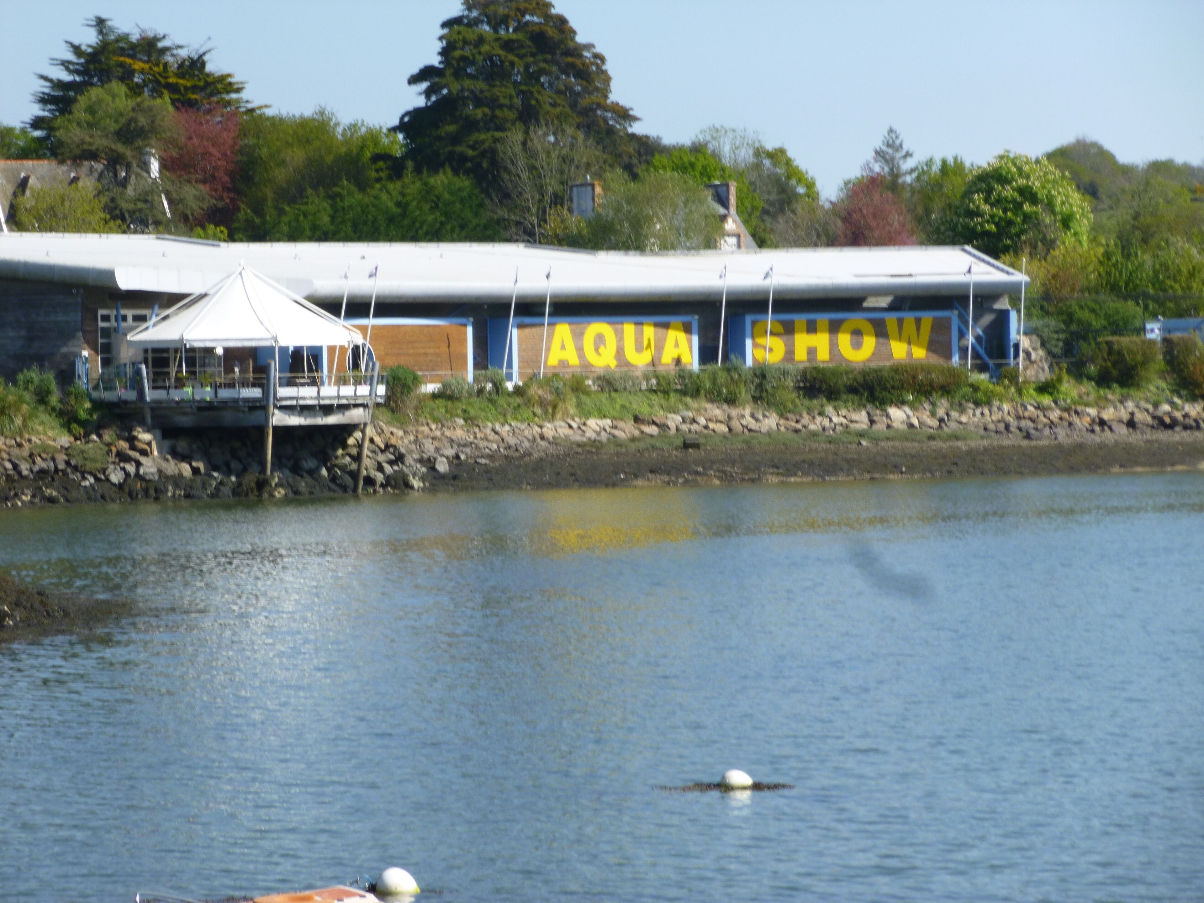 Un bâtiment portant l’inscription « AQUA SHOW », un quai doté d’une zone abritée et une étendue d’eau calme.