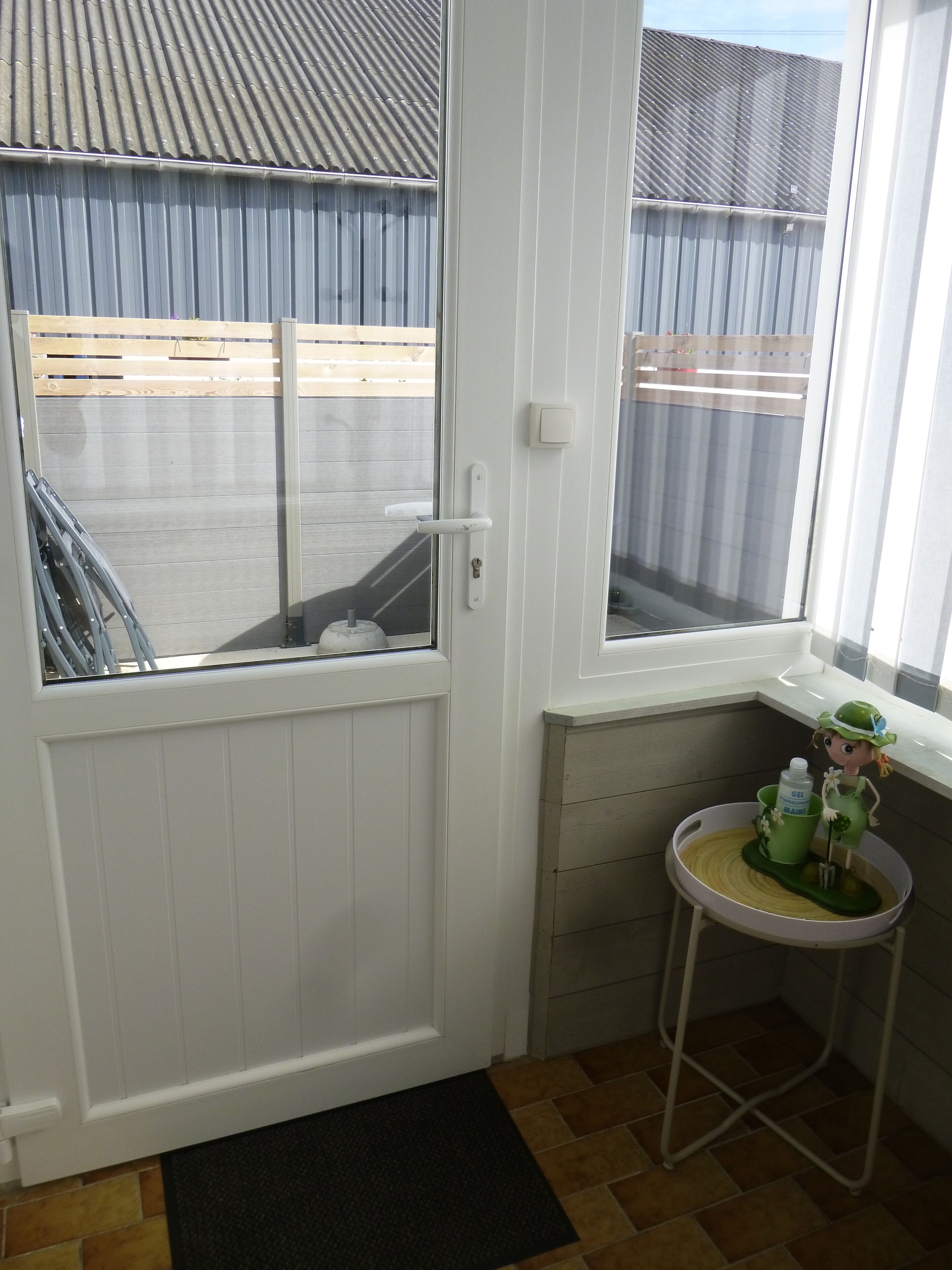 A white door with a window, a small stool with a green mat, and a white wall with a light switch.