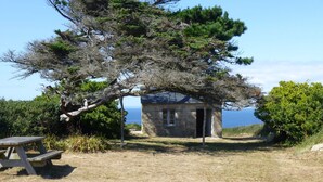 Un edificio de piedra con un porche pequeño, rodeado de árboles y una mesa de picnic.