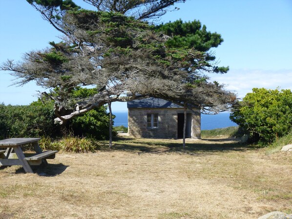 A stone building with a small porch, surrounded by trees and a picnic table.