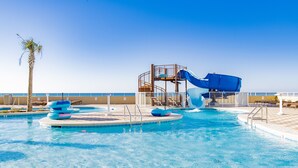Une piscine avec un toboggan, des palmiers et des chaises longues.