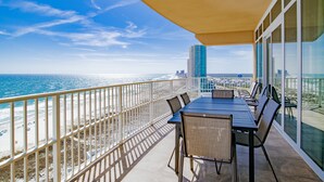 Un balcon avec vue sur la plage et l’océan, une table avec des chaises et une rambarde en verre.