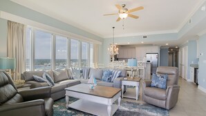 Un vaste salon avec vue sur l’océan, doté d’un ventilateur de plafond et d’un lustre.