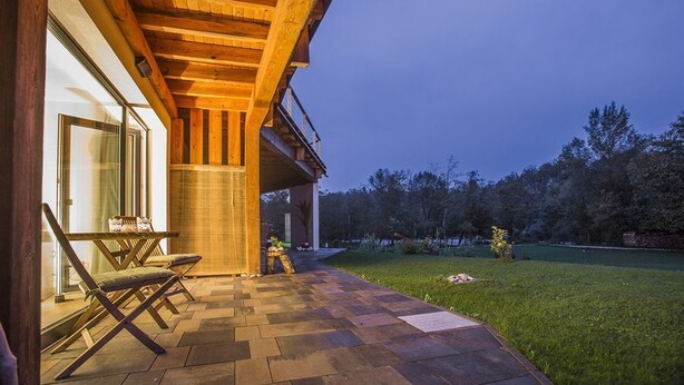 Un espace extérieur abrité, doté d’un plafond en bois, d’une porte vitrée donnant sur l’intérieur et d’une terrasse dallée.