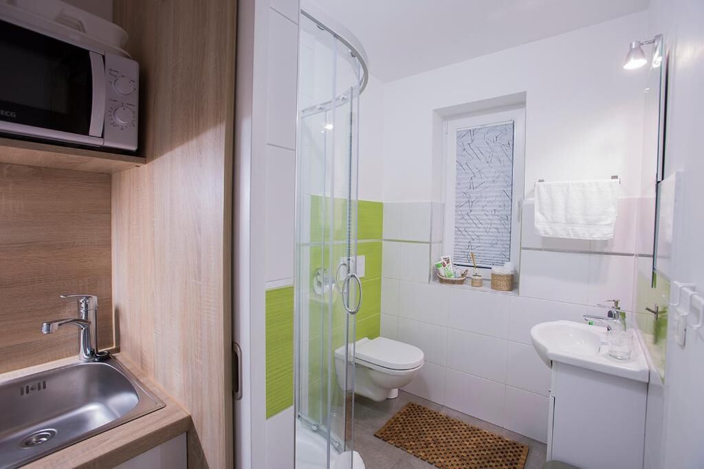 A modern bathroom with a glass shower enclosure, a toilet, a sink, and a microwave above the sink.