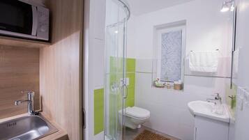 A modern bathroom with a glass shower enclosure, a toilet, a sink, and a microwave above the sink.