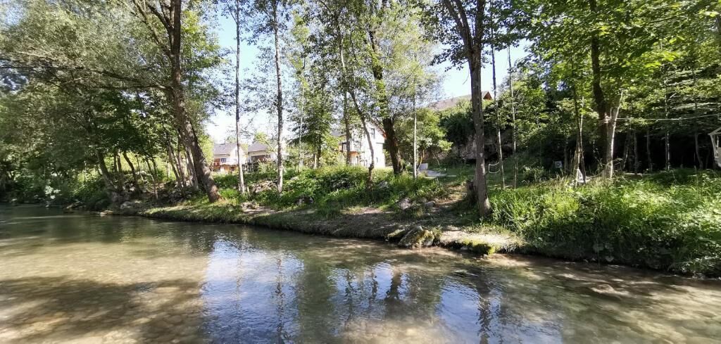 A calm river with trees and a house in the background.
