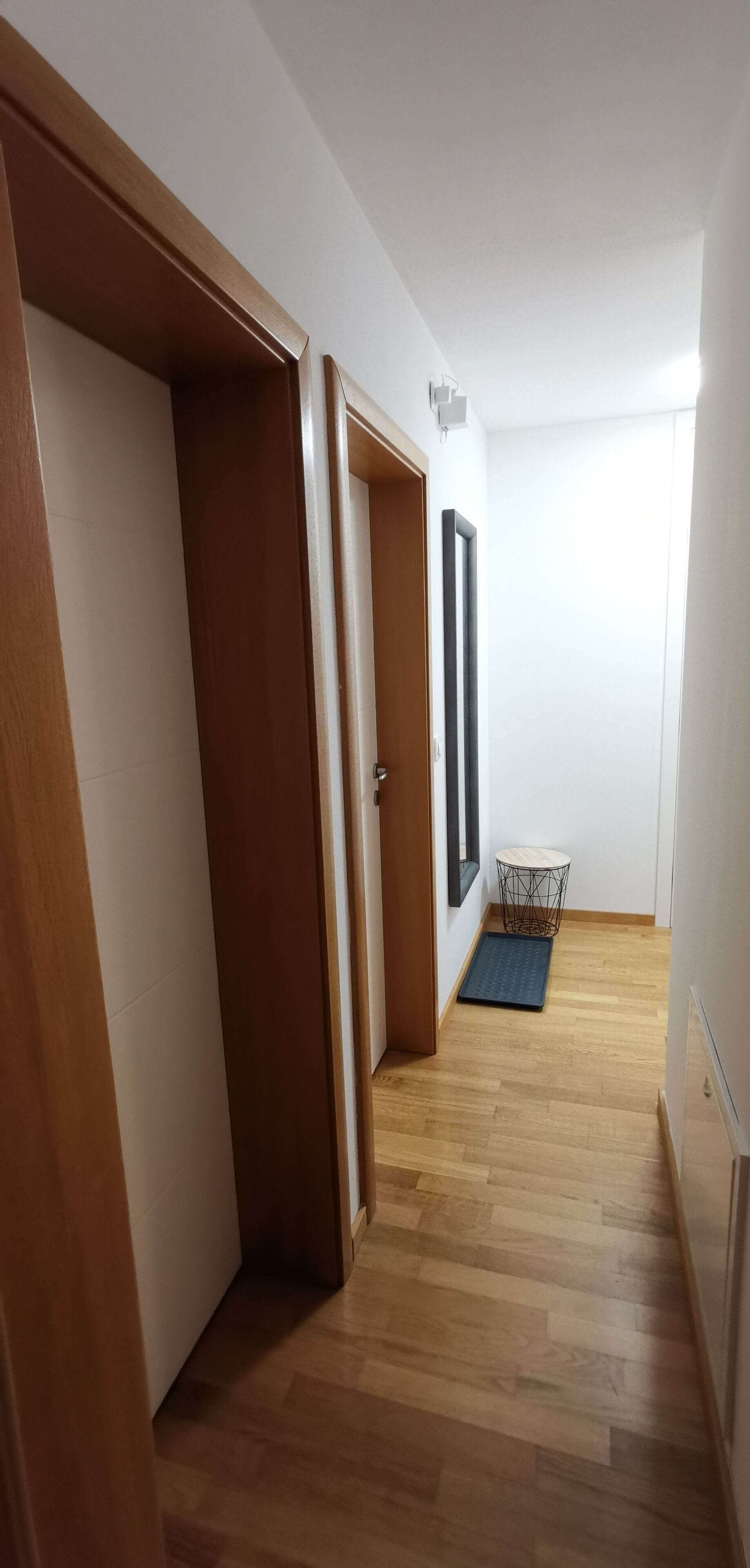 Un corridoio con pavimento in legno, pareti bianche e una porta che dà su una stanza.