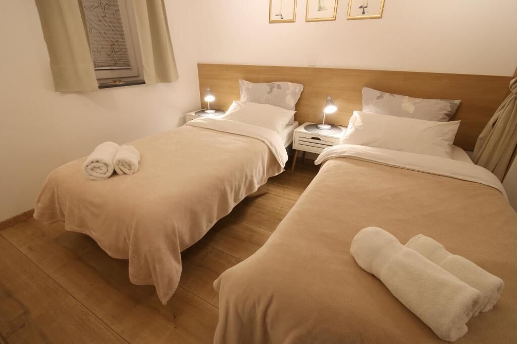 Habitación doble con dos camas, cada una con mesita de noche y lámpara, y una ventana con cortinas.