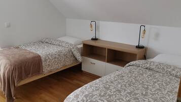 A bedroom with two single beds, a wooden nightstand, and two wall-mounted reading lamps.