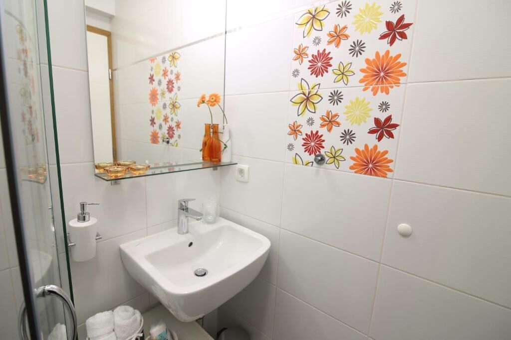 A bathroom with a white sink, glass shelves, a mirror, and a floral tile backsplash.