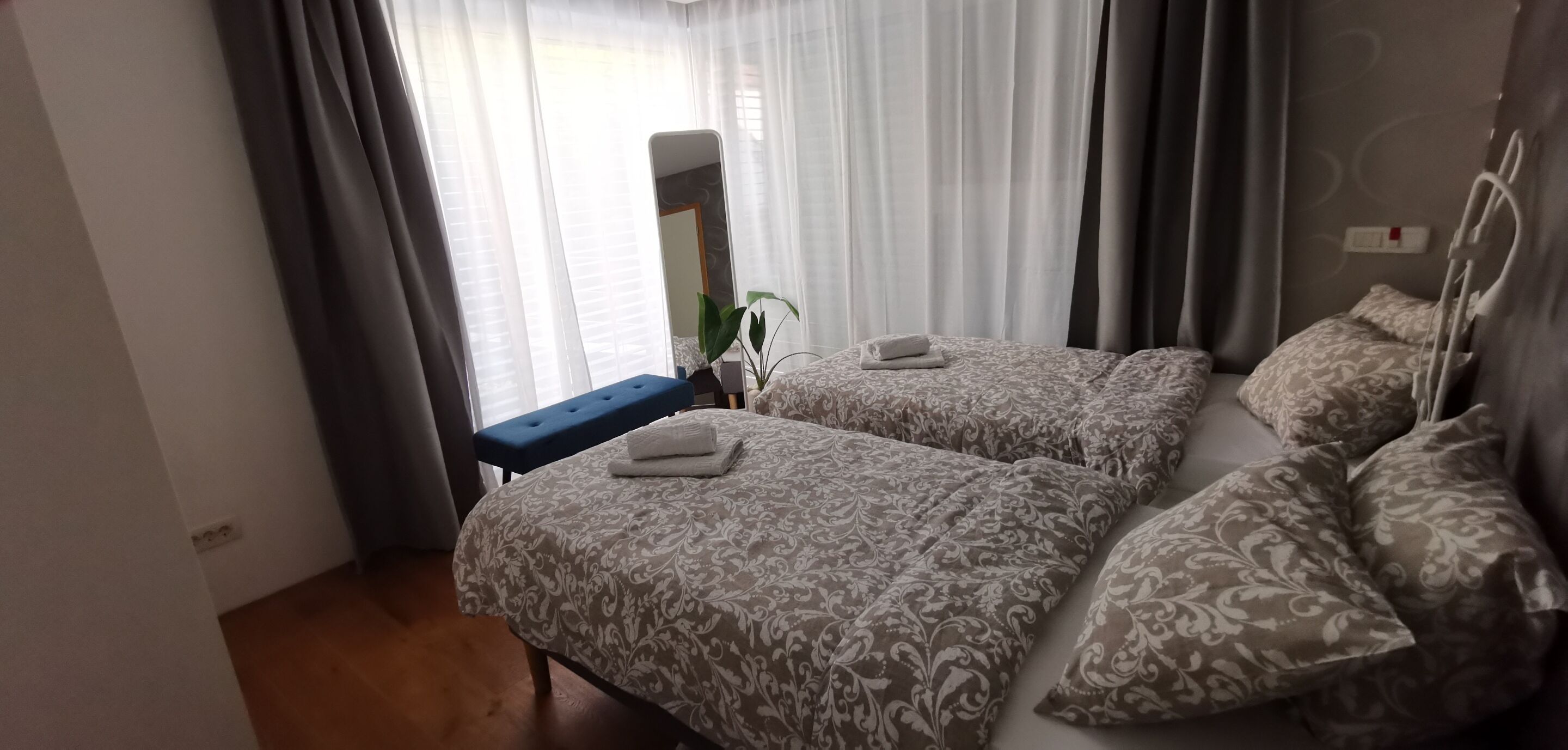 A hotel room with two beds, a bench, and a bedside table.