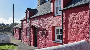 A red-painted building with a stone facade, a chimney, and a small window. - 2 bedroom accommodation in Morfa Nefyn (Morfa Nefyn)