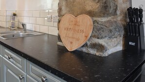 A kitchen with a stone wall, a heart-shaped wooden sign, a knife block, and a sink. - 2 bedroom accommodation in Morfa Nefyn (Morfa Nefyn)