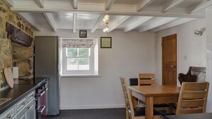A compact kitchen with a dining area, stone wall, and a window with a view. - 2 bedroom accommodation in Morfa Nefyn (Morfa Nefyn)