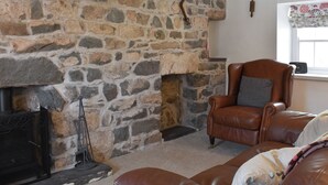 A stone fireplace, leather armchair, and a dog resting on a couch in a cozy living room. - 2 bedroom accommodation in Morfa Nefyn (Morfa Nefyn)
