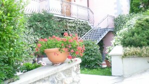 A building with a stone wall, a large potted plant with red flowers, and a metal staircase leading to a door. - Apartment/ flat - Sermezzana (Minucciano)