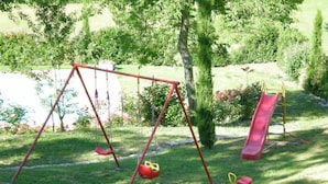 A playground with swings and a slide in a grassy area with trees and bushes. - Apartment/ flat - Sermezzana (Minucciano)