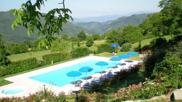 A pool area with blue umbrellas and lounge chairs, surrounded by lush greenery and hills in the background. - Apartment/ flat - Sermezzana (Minucciano)