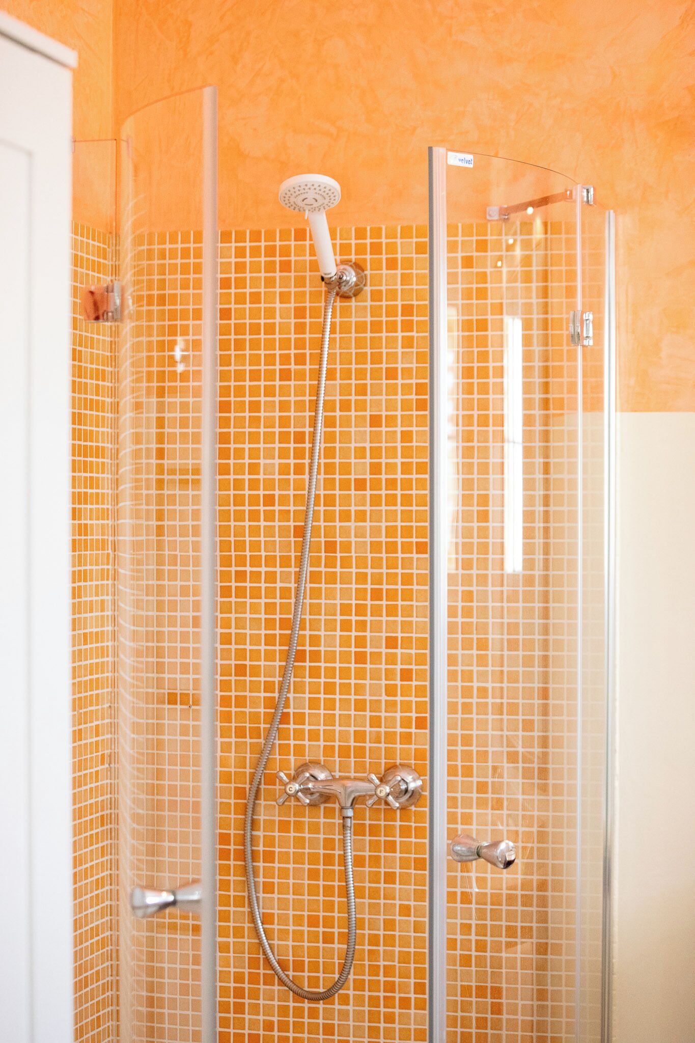 A shower with a glass enclosure, a handheld showerhead, and a handheld faucet.
