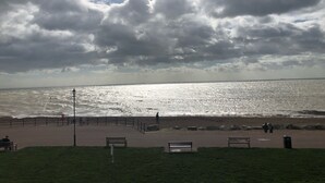 A beach with a paved walkway, benches, and a fence separating the path from the water. - Stunning Sea Front Apartment (Hythe)