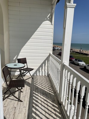 A balcony with a white railing, a round table, and two wicker chairs. - Stunning Sea Front Apartment (Hythe)