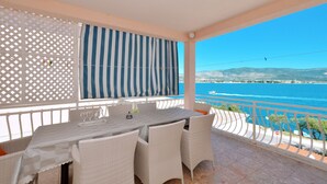 A balcony with a table and chairs, overlooking a coastal view.