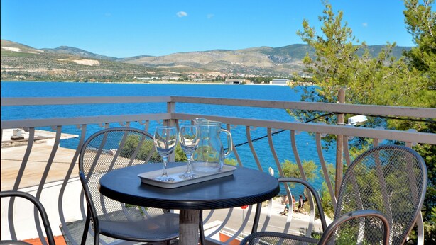 A balcony with a table and chairs overlooking a body of water and distant hills.