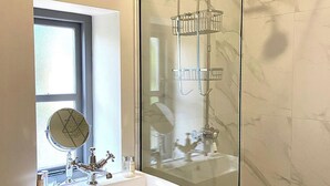 Un baño con ducha envuelta en vidrio, lavamanos con espejo y ventana.