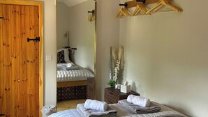 Un dormitorio con puerta de madera, una cama con toallas ordenadas, un espejo y un perchero de madera fijado a la pared.
