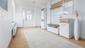 Una habitación moderna y bien iluminada con una puerta blanca, un armario blanco con tapa de madera, un florero blanco y un radiador blanco.