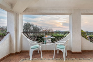 A balcony with two white chairs and a table, overlooking a garden and a sunset. - Apartment Villa Nera (Pula)