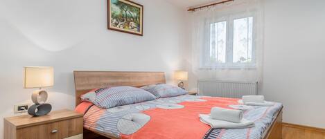Un dormitorio ordenado con cama, mesitas de noche, una ventana con cortinas y un cuadro en la pared.