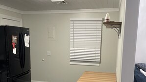 Eine kleine Küche mit einem schwarzen Kühlschrank, einem Holztisch und einem Fenster mit Jalousien.